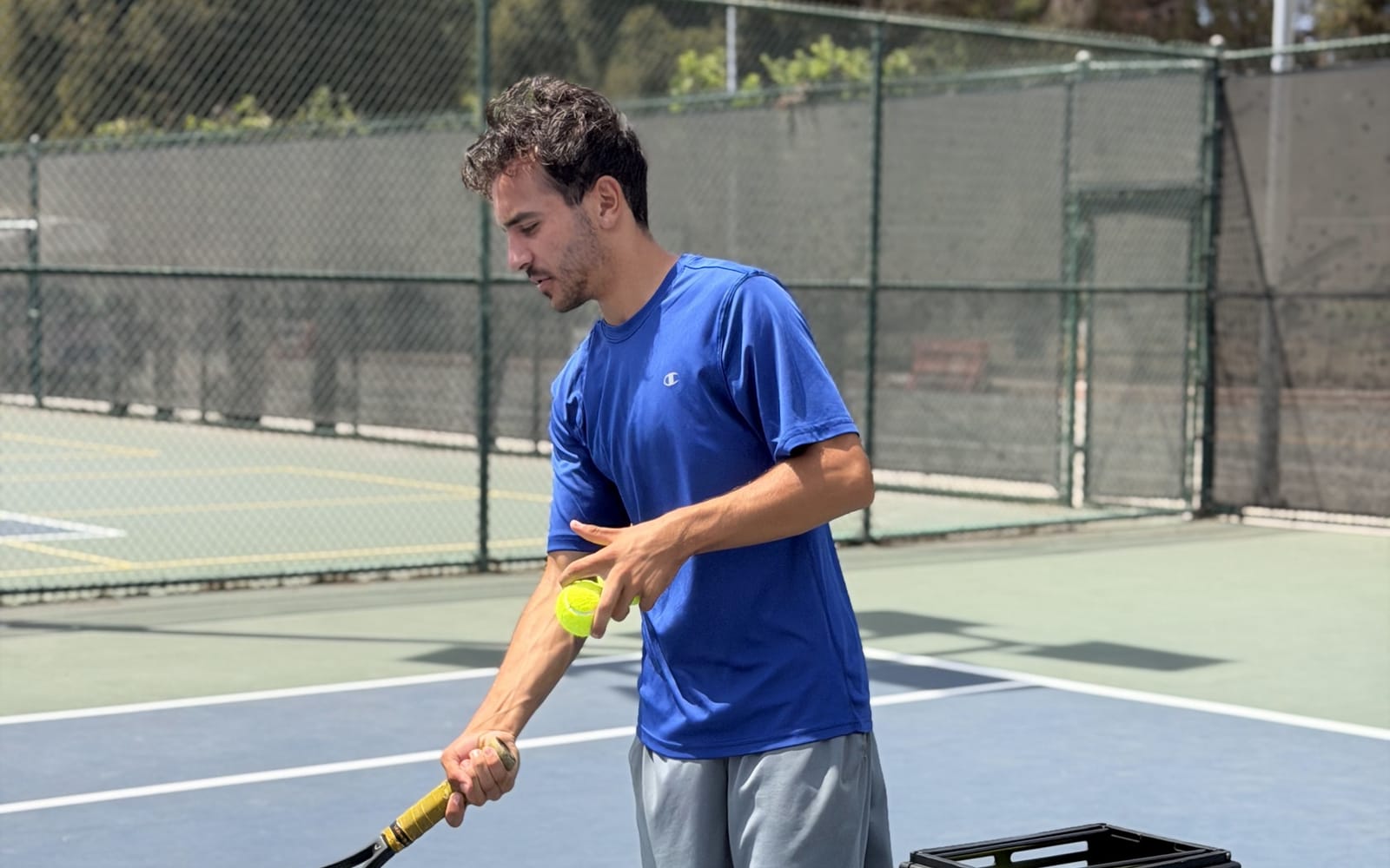 Adult tennis lesson on a Los Angeles court — coach feeding from a ball basket