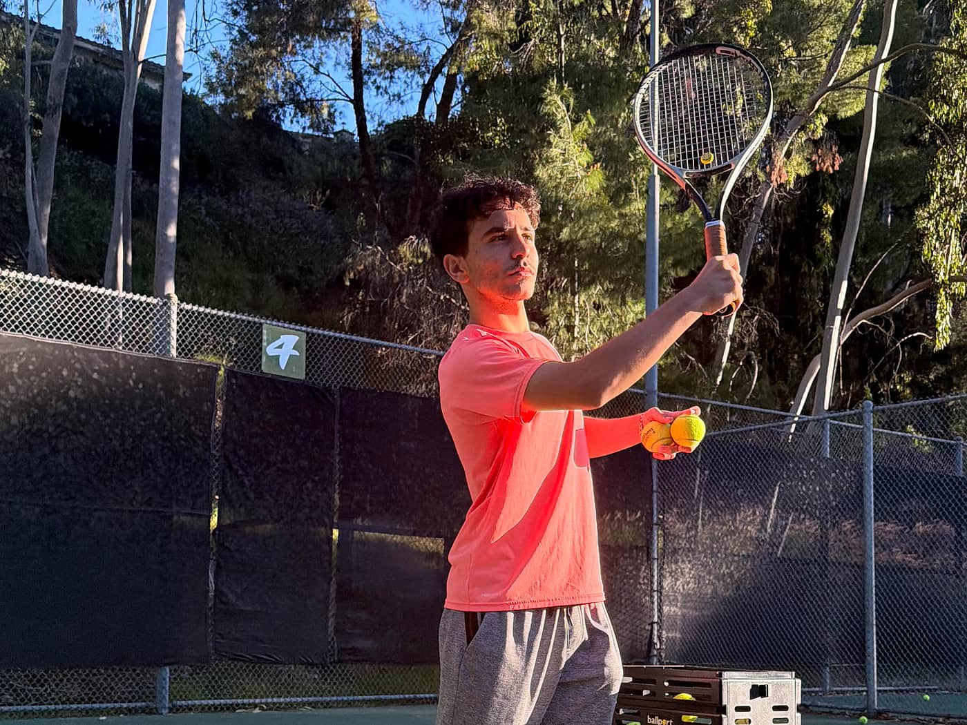 A tennis coach feeding balls from a basket during a lesson in Pasadena, California